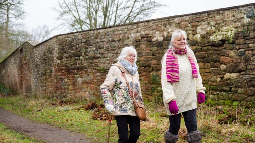 Two people smiling mid-sentence walking through the estate at Acorn Bank, Cumbria